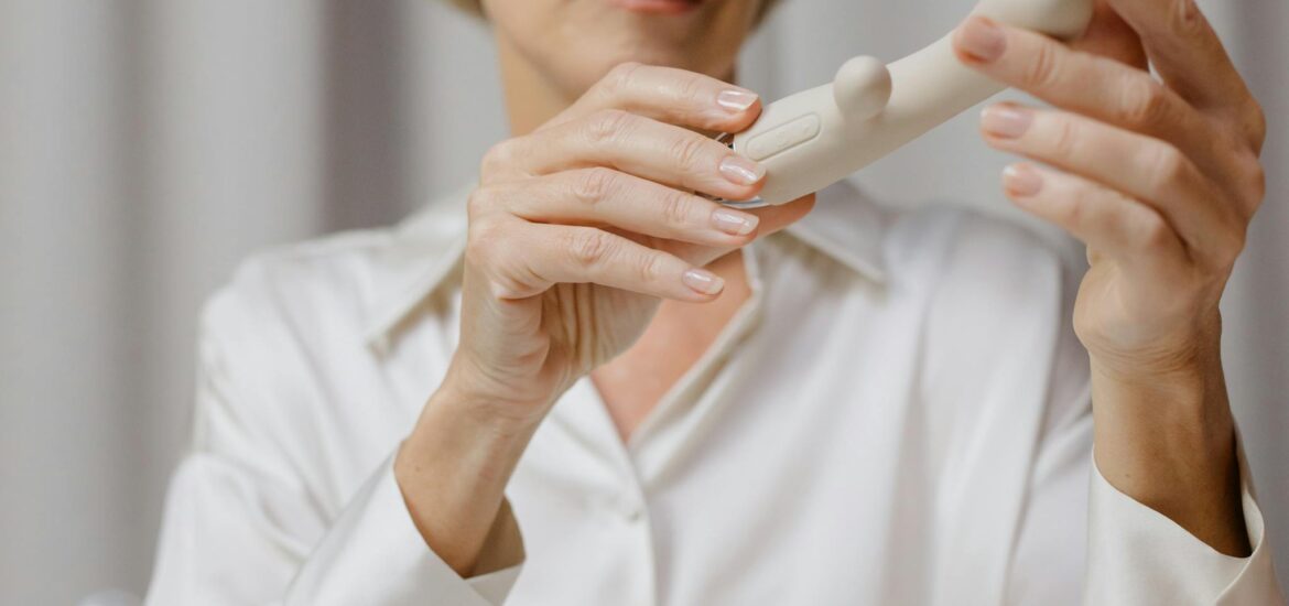 A mature woman examines a cream-colored personal wellness device indoors.