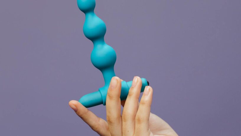 Close-up of a hand holding a purple silicone toy against a purple background.